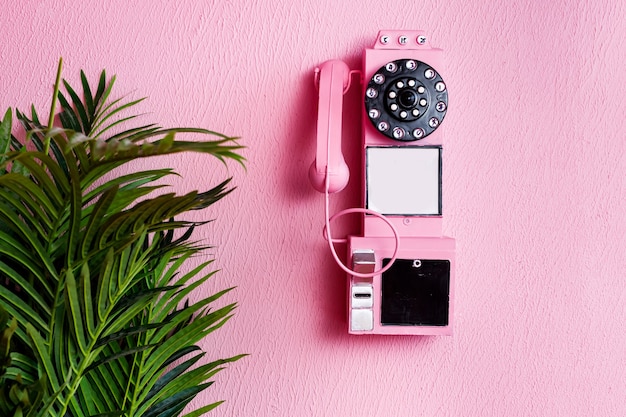 Foto teléfono tradicional antiguo rosa con receptor sobre fondo rosa pastel y planta verde con espacio de copia