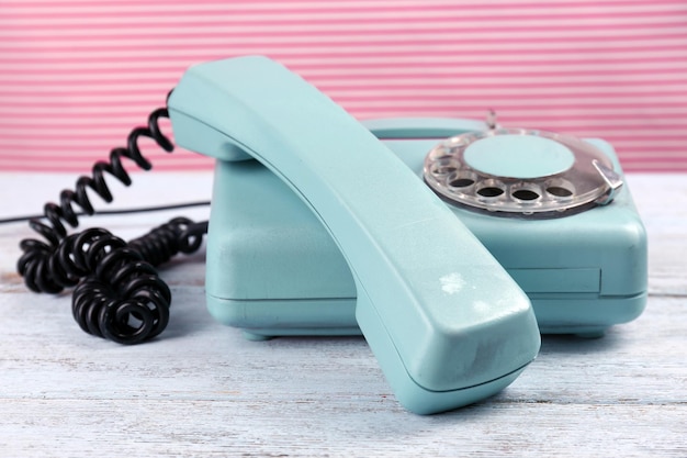 Teléfono turquesa retro sobre mesa de madera sobre fondo de color