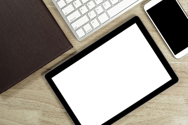 Teléfonos inteligentes de pantalla en blanco y tableta en el escritorio de madera y teclado blanco