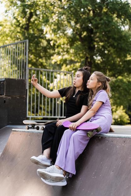 Telefonsüchtige Sportkinder mit Skateboard und Penny Boards benutzen Telefone und machen Selfies, anstatt zu skaten und zusammen zu spielen Kinder, die Smartphones auf Sportrampe betrachten Telefonsucht