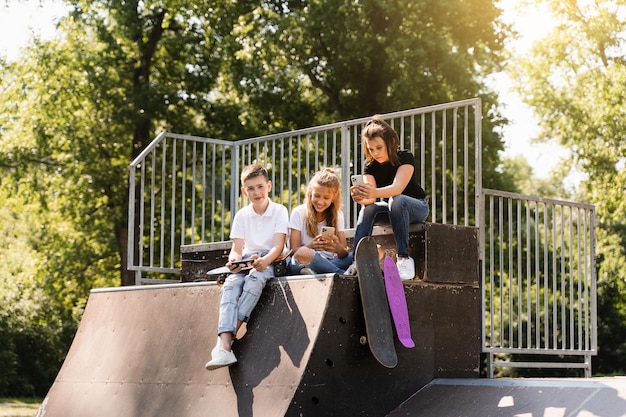 Telefonsüchtige Sportkinder mit Skateboard und Penny Boards verwenden Telefone, anstatt zu skaten und zusammen zu spielen Kinder, die Smartphones auf einer Sportrampe betrachten