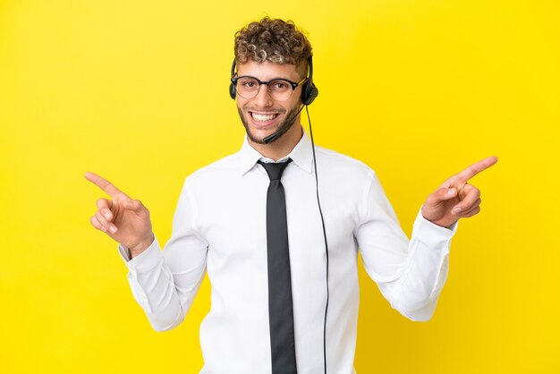 Telemarketer blonder Mann, der mit einem Headset arbeitet, das auf gelbem Hintergrund isoliert ist und mit dem Finger auf die Seitenwände zeigt und glücklich ist