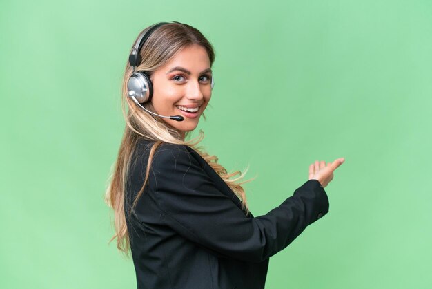 Telemarketer bonita mujer uruguaya trabajando con un auricular sobre un fondo aislado apuntando hacia atrás