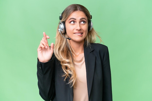 Telemarketer bonita mujer uruguaya trabajando con un auricular sobre un fondo aislado con los dedos cruzados y deseando lo mejor