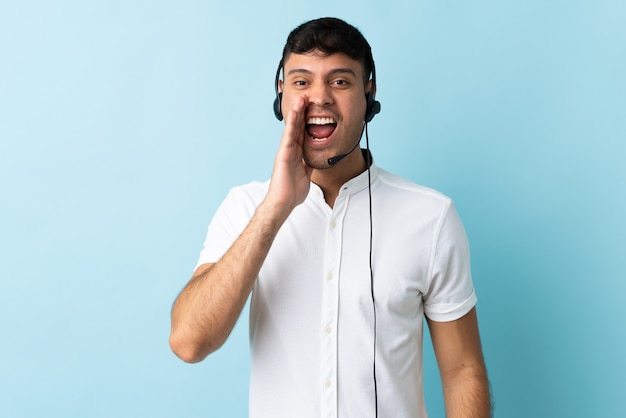 Telemarketer colombiano hombre trabajando con un auricular sobre gritos aislados con la boca abierta