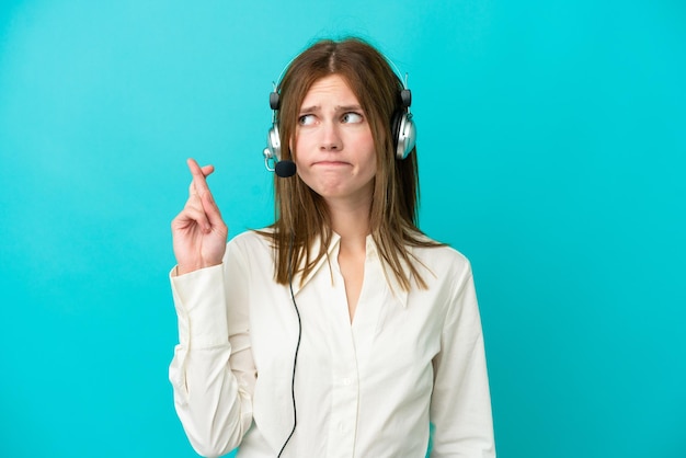 Telemarketer Engländerin, die mit einem Headset arbeitet, das auf blauem Hintergrund isoliert ist, die Daumen drückt und das Beste wünscht