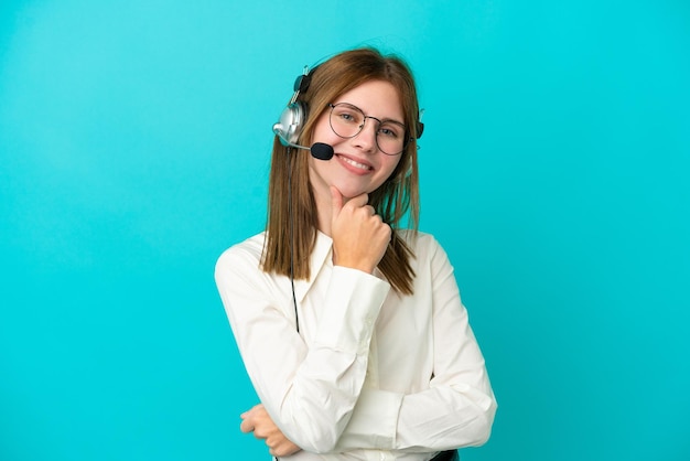 Telemarketer Engländerin, die mit einem Headset arbeitet, isoliert auf blauem Hintergrund, mit Brille und lächelnd