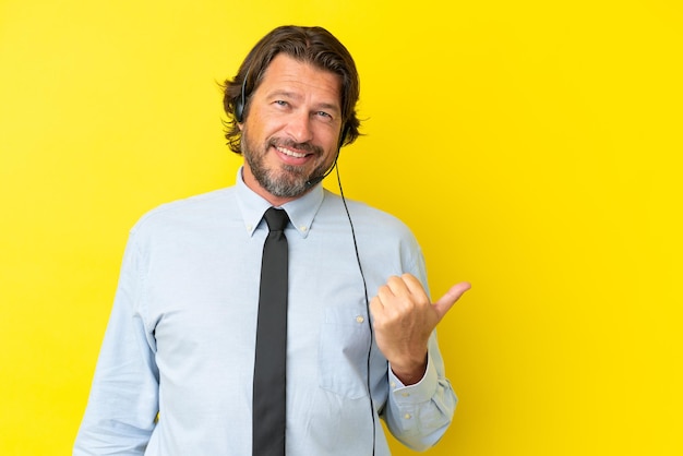 Telemarketer holländischer Mann, der mit einem Headset arbeitet, das auf gelbem Hintergrund isoliert ist und auf die Seite zeigt, um ein Produkt zu präsentieren