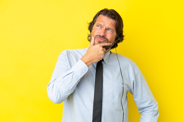 Telemarketer holländischer Mann, der mit einem Headset arbeitet, das auf gelbem Hintergrund isoliert ist, Zweifel hat und mit verwirrendem Gesichtsausdruck