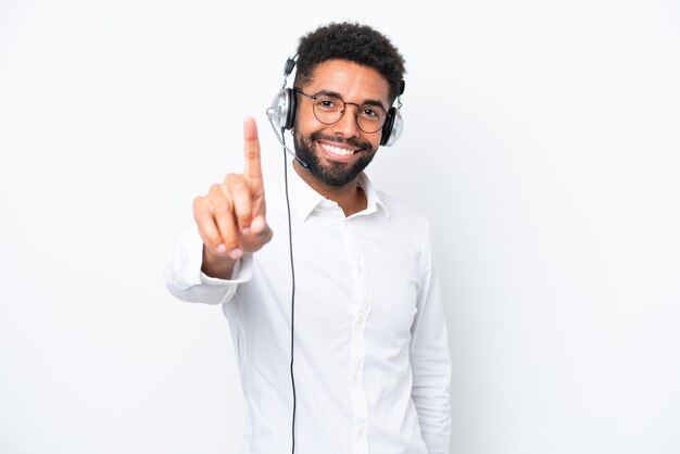 Telemarketer hombre brasileño trabajando con un auricular aislado sobre fondo blanco mostrando y levantando un dedo