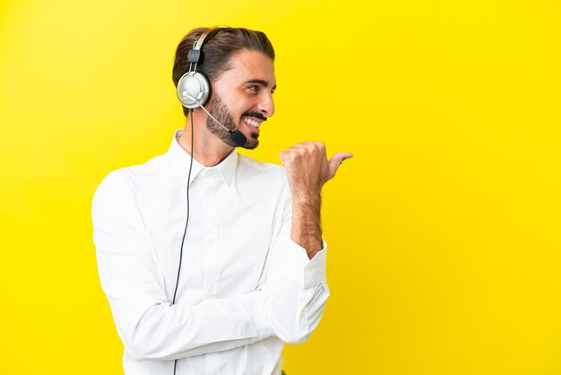 Telemarketer hombre caucásico que trabaja con un auricular aislado sobre fondo amarillo apuntando hacia un lado para presentar un producto