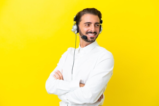 Telemarketer hombre caucásico que trabaja con un auricular aislado sobre fondo amarillo con los brazos cruzados y feliz