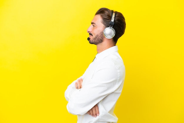 Telemarketer hombre caucásico que trabaja con un auricular aislado sobre fondo amarillo en posición lateral