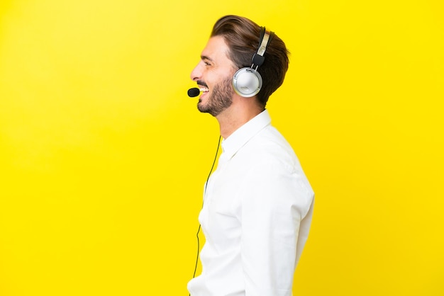 Telemarketer hombre caucásico que trabaja con un auricular aislado sobre fondo amarillo riendo en posición lateral