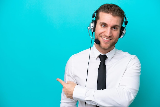 Telemarketer hombre caucásico que trabaja con un auricular aislado sobre fondo azul apuntando hacia atrás