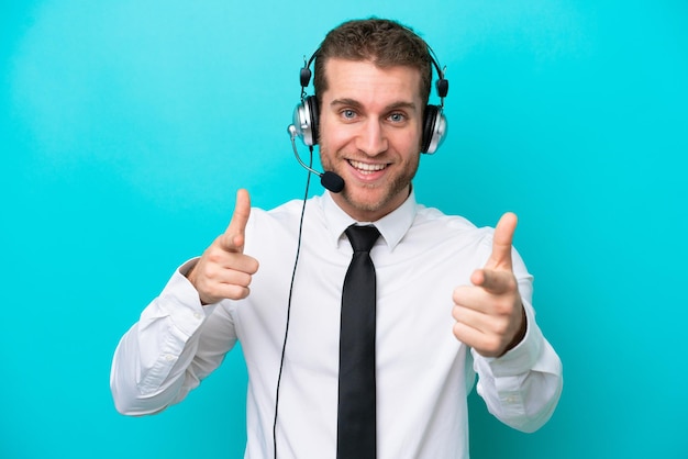 Telemarketer hombre caucásico que trabaja con un auricular aislado sobre fondo azul apuntando hacia el frente y sonriendo