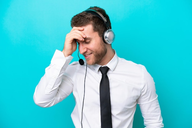 Telemarketer hombre caucásico que trabaja con un auricular aislado sobre fondo azul riendo