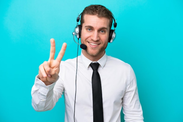 Telemarketer hombre caucásico que trabaja con un auricular aislado sobre fondo azul sonriendo y mostrando el signo de la victoria