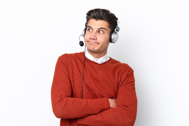 Telemarketer hombre caucásico que trabaja con un auricular aislado sobre fondo blanco haciendo gesto de dudas mientras levanta los hombros