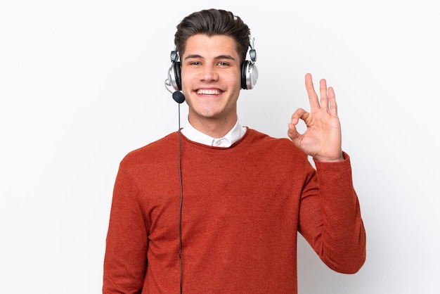 Telemarketer hombre caucásico que trabaja con un auricular aislado sobre fondo blanco que muestra el signo de ok con los dedos