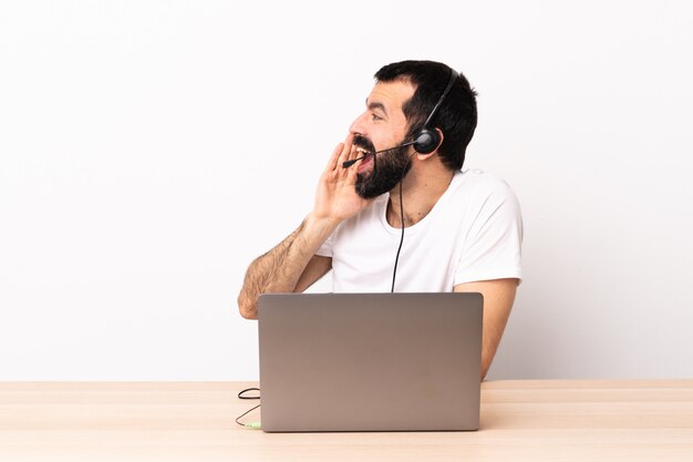 Telemarketer hombre caucásico que trabaja con auriculares y con laptop gritando con la boca abierta a un lado