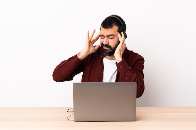 Telemarketer hombre caucásico que trabaja con auriculares y portátil con dolor de cabeza