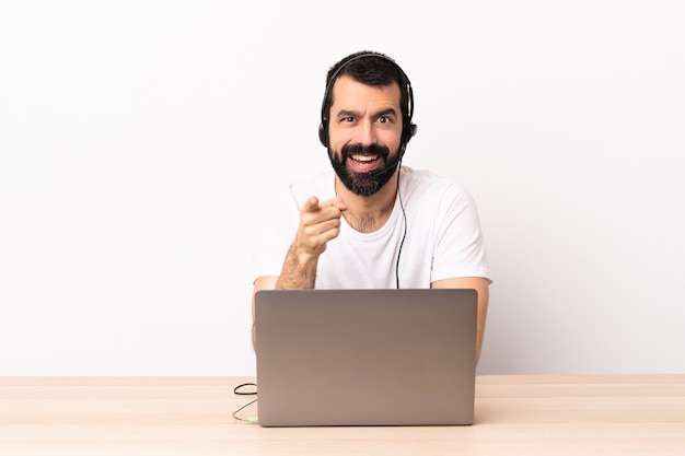 Telemarketer hombre caucásico trabajando con auriculares y con portátil sorprendido y apuntando al frente