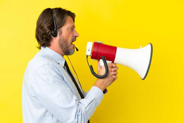 Telemarketer hombre holandés que trabaja con un auricular aislado sobre fondo amarillo gritando a través de un megáfono