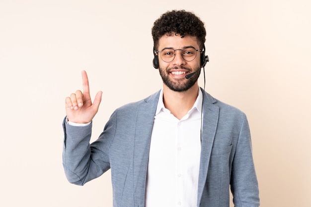 Telemarketer hombre marroquí que trabaja con un auricular aislado en beige apuntando hacia una gran idea