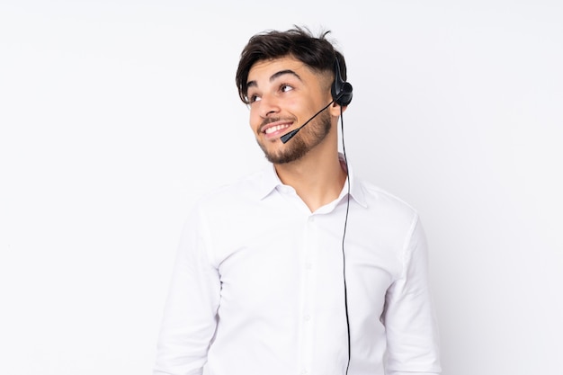 Telemarketer hombre trabajando con un auricular aislado en la pared blanca riendo y mirando hacia arriba