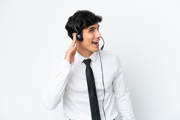 Telemarketer hombre trabajando con un auricular aislado sobre fondo blanco escuchando algo poniendo la mano en la oreja