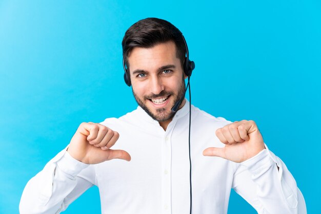 Telemarketer hombre trabajando con un auricular sobre azul orgulloso y satisfecho de sí mismo