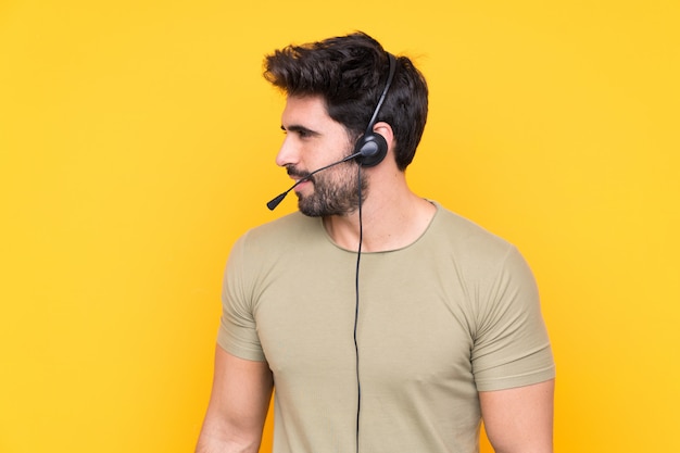 Telemarketer hombre trabajando con un auricular sobre pared amarilla aislada mirando hacia el lado