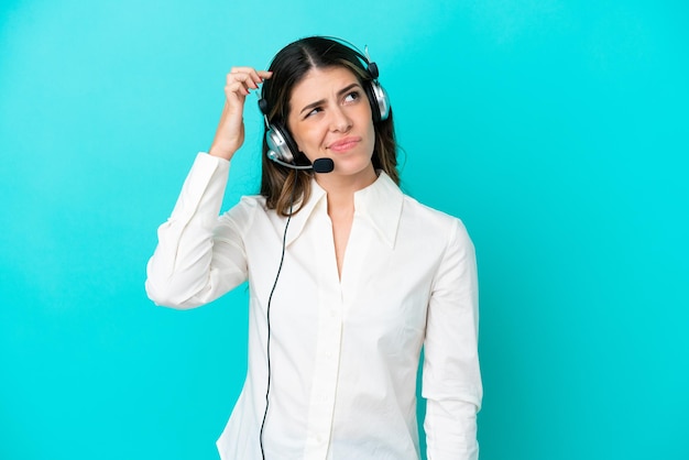 Telemarketer-Italienerin, die mit einem Headset arbeitet, isoliert auf blauem Hintergrund, hat Zweifel und verwirrten Gesichtsausdruck