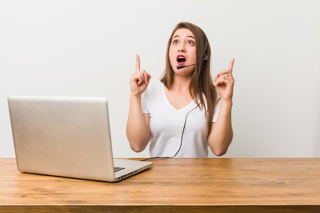 Telemarketer joven mujer apuntando al revés con la boca abierta.