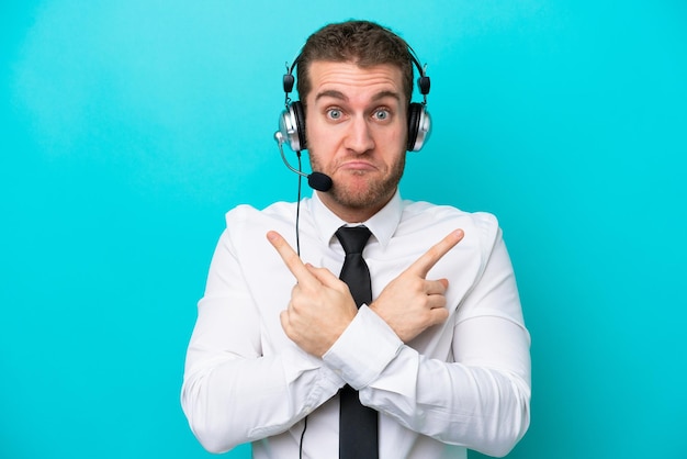 Telemarketer kaukasischer Mann, der mit einem Headset arbeitet, das auf blauem Hintergrund isoliert ist und auf die Seiten zeigt, die Zweifel haben