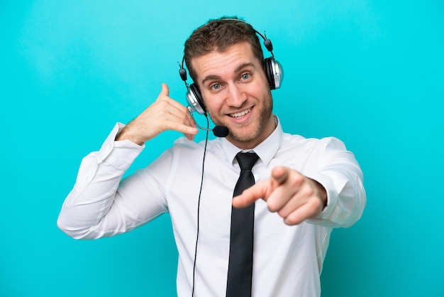 Telemarketer kaukasischer Mann, der mit einem Headset arbeitet, das auf blauem Hintergrund isoliert ist und eine Telefongeste macht und nach vorne zeigt