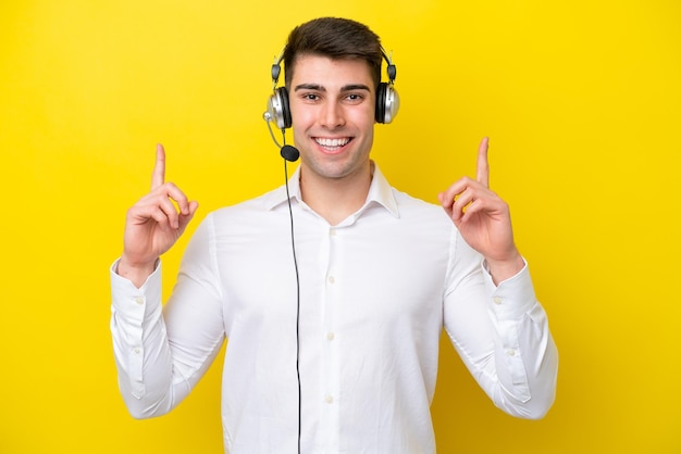 Telemarketer kaukasischer Mann, der mit einem Headset arbeitet, das auf gelbem Hintergrund isoliert ist und auf eine großartige Idee zeigt