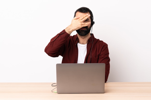 Telemarketer kaukasischer Mann, der mit einem Headset und mit Laptop arbeitet, der Augen durch Hände und Lächeln kegelt.