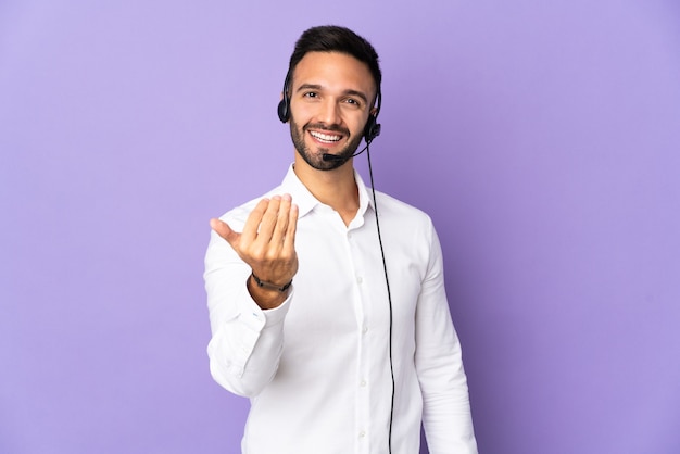 Telemarketer-Mann, der mit einem Headset arbeitet, das auf lila Hintergrund lokalisiert wird, der einlädt, mit Hand zu kommen. Schön, dass du gekommen bist