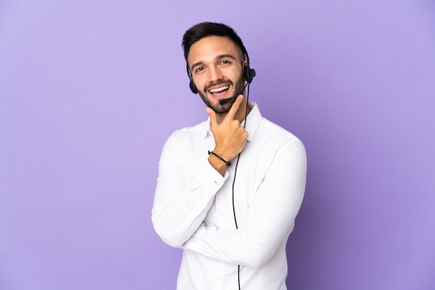 Telemarketer-Mann, der mit einem Headset arbeitet, lokalisiert auf lila Hintergrund glücklich und lächelnd