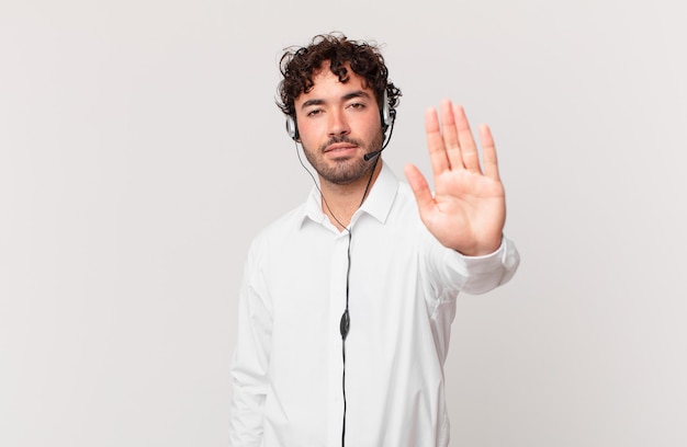 Telemarketer mirando serio, severo, disgustado y enojado mostrando la palma abierta haciendo gesto de parada