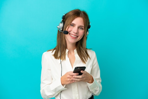 Telemarketer mujer inglesa trabajando con un auricular aislado sobre fondo azul enviando un mensaje con el móvil