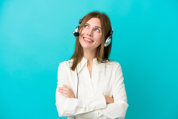 Telemarketer mujer inglesa trabajando con un auricular aislado sobre fondo azul mirando hacia arriba mientras sonríe