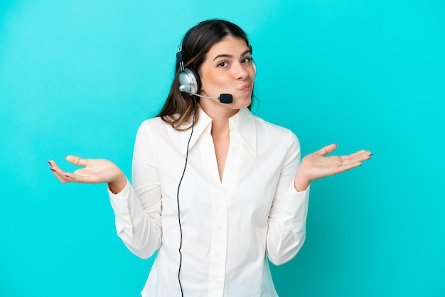 Telemarketer Mujer italiana que trabaja con un auricular aislado de fondo azul que tiene dudas mientras levanta las manos