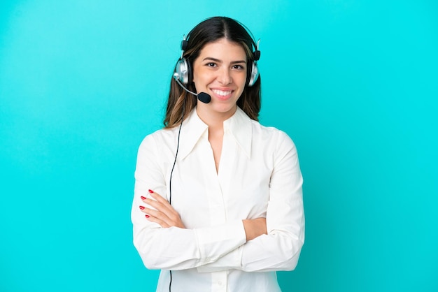 Telemarketer mujer italiana que trabaja con un auricular aislado sobre fondo azul manteniendo los brazos cruzados en posición frontal