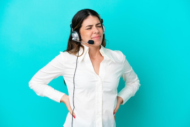 Telemarketer mujer italiana que trabaja con un auricular aislado sobre fondo azul que sufre de dolor de espalda por haber hecho un esfuerzo