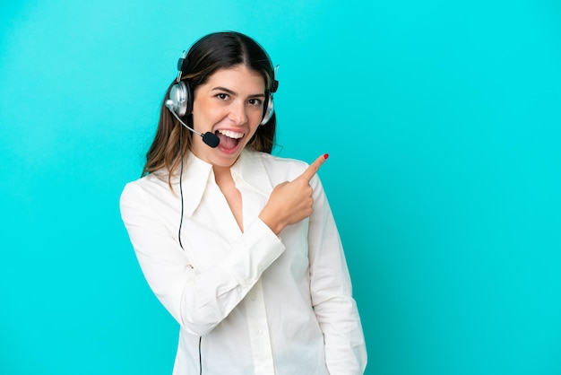 Telemarketer mujer italiana que trabaja con un auricular aislado sobre fondo azul sorprendido y apuntando hacia el lado