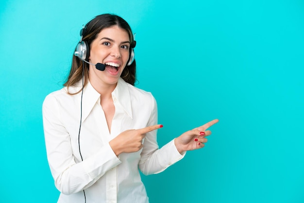 Telemarketer mujer italiana que trabaja con un auricular aislado sobre fondo azul sorprendido y apuntando hacia el lado