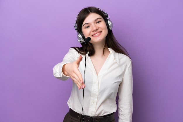 Telemarketer Mujer rusa que trabaja con un auricular aislado en un fondo morado dándose la mano para cerrar un buen trato